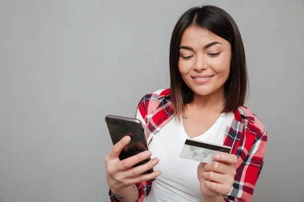 Mujer feliz sosteniendo la tarjeta de crédito y el uso de teléfono móvil —  Fotos de Stock