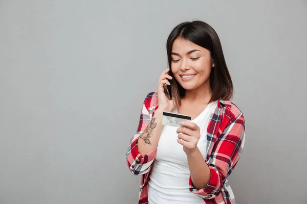 Mujer sonriente sosteniendo tarjeta de crédito y hablando por teléfono móvil — Foto de Stock