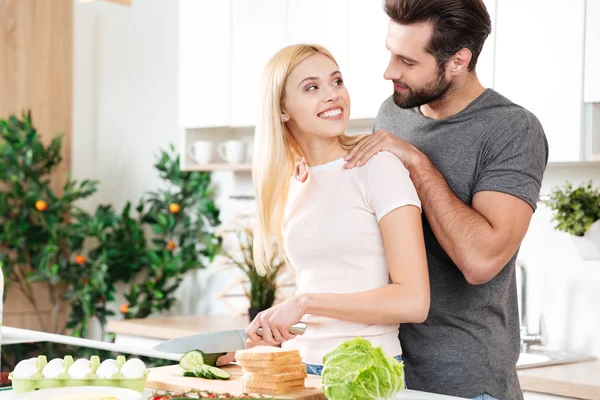 Happy young loving couple standing at kitchen and cooking — Stock Photo, Image