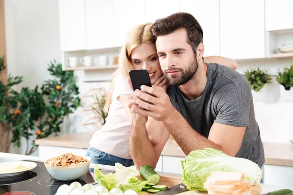 Happy smiling couple using mobile phone to find a recipe