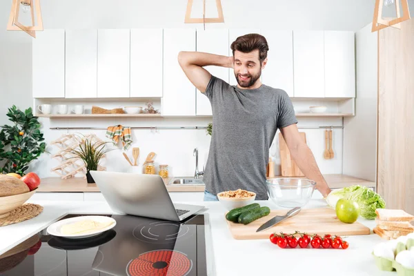 Homem bonito confuso cozinhar salada de legumes na cozinha — Fotografia de Stock