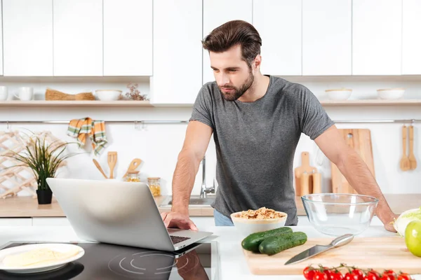 Мужчина ищет рецепт на ноутбуке на кухне дома — стоковое фото