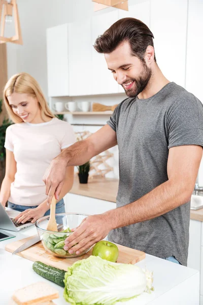 Sorrindo jovem casal amoroso cozinhar juntos usando laptop — Fotografia de Stock