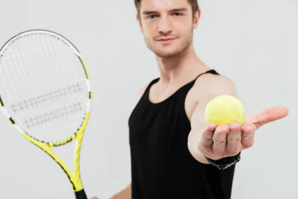 Pohledný mladý sportovec drží tenisák a raketa — Stock fotografie