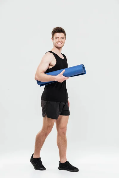 Happy young sportsman holding fitness rug — Stock Photo, Image