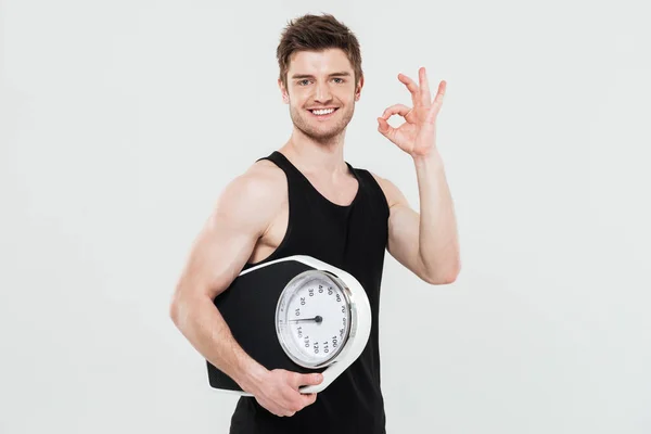 Jovem desportista feliz segurando escalas mostrando gesto ok — Fotografia de Stock