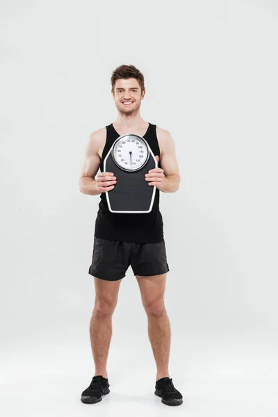 Cheerful young sportsman holding scales — Stock Photo, Image