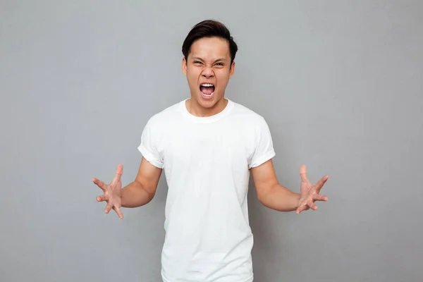 Skrikande ung asiatisk man står över grå bakgrund — Stockfoto