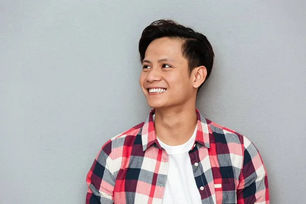 Jovem sorrindo asiático homem de pé sobre cinza parede . — Fotografia de Stock