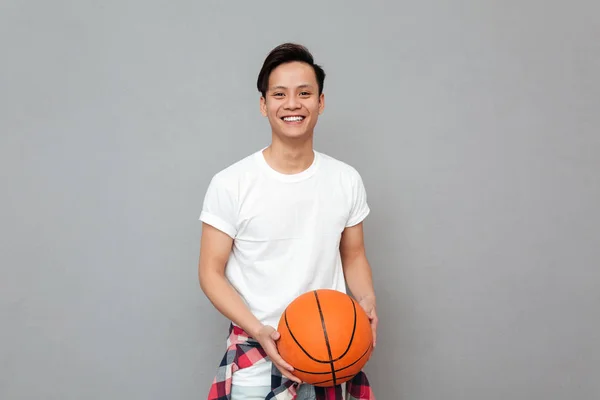 Feliz joven asiático hombre sobre gris fondo con cesta bola —  Fotos de Stock