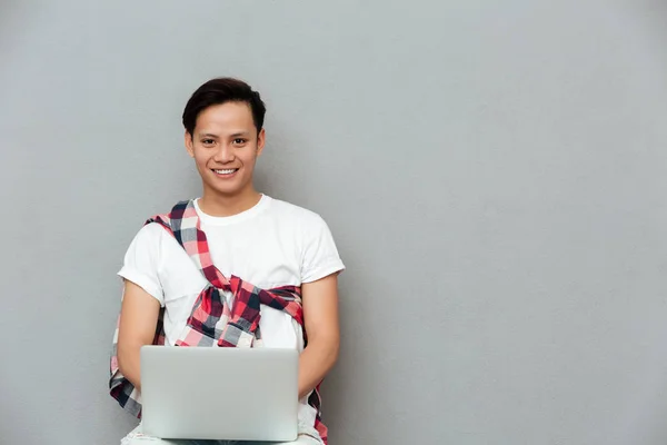 Feliz joven asiático hombre sobre gris fondo usando portátil —  Fotos de Stock