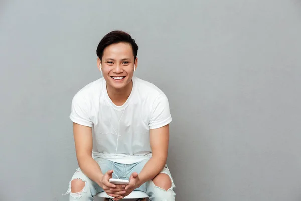 Alegre joven asiático hombre sobre gris fondo escuchar música —  Fotos de Stock