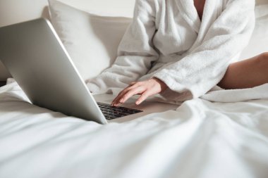 Bir kadının yatak ve dizüstü bilgisayar kullanarak bornoz içinde kırpılmış görüntü