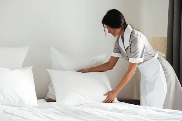 Joven sirvienta del hotel instalando almohada en la cama — Foto de Stock