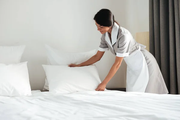 Young hotel maid setting up pillow on bed — Stock Photo, Image