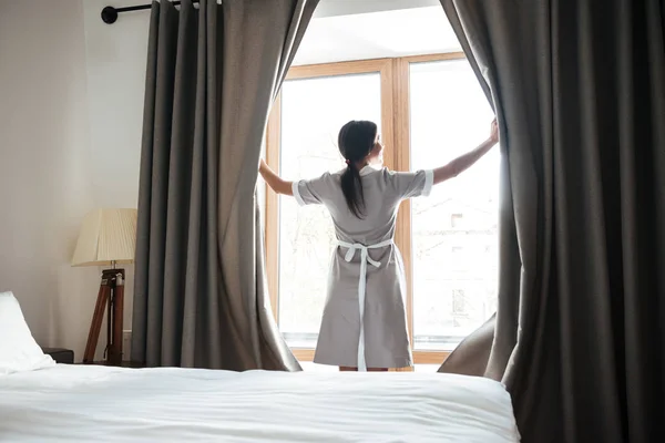 Camareira fêmea cortinas janela de abertura no quarto do hotel — Fotografia de Stock