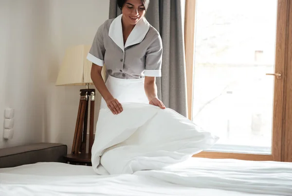 Maid setting up white bed sheet in hotel room — Stock Photo, Image