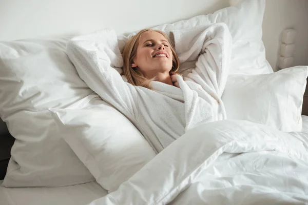 Joven mujer feliz tumbada en la cama blanca grande —  Fotos de Stock