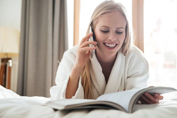 Giovane donna bionda che legge la rivista e parla al telefono — Foto Stock