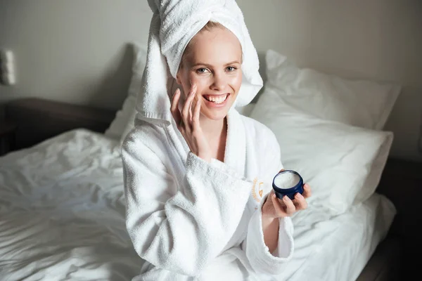 Щаслива усміхнена жінка в халаті кладе крем на обличчя — стокове фото