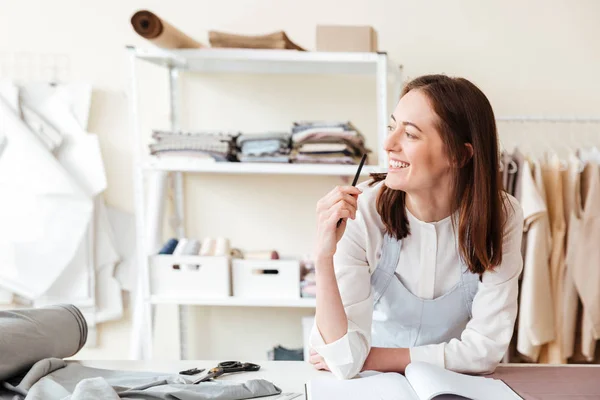 Mulher sorridente costureira com lápis olhando para o lado — Fotografia de Stock