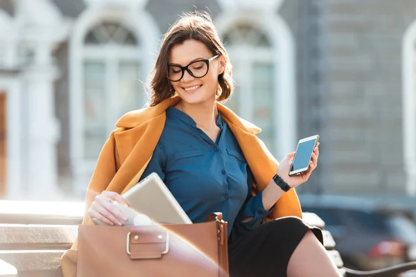 Mujer bonita sonriente en gafas y abrigo con teléfono móvil —  Fotos de Stock