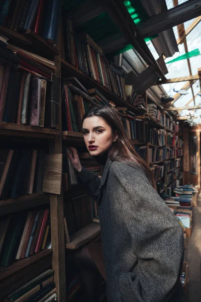 Mulher na moda subindo em uma escada em um armazém de livro — Fotografia de Stock