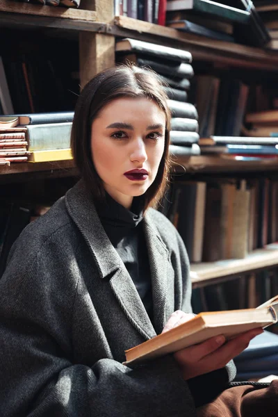 Junges Mädchen im Mantel hält Buch in einer alten Bibliothek — Stockfoto