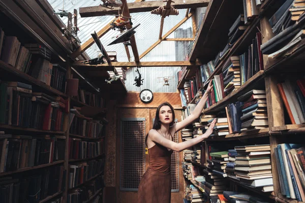 Junges brünettes Mädchen steht zwischen Büchern — Stockfoto