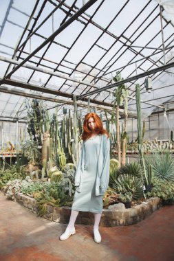 Genç kız camdan bir evde ayakta kaktüsler dolu