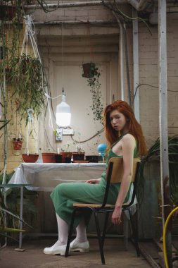 Bitkiler arasında sandalye üzerinde oturan kız