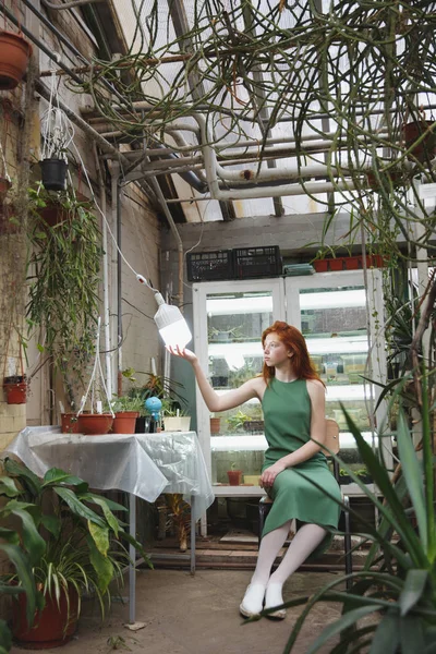 Girl sitting near table in greenery and looking at lamp — Stock Photo, Image