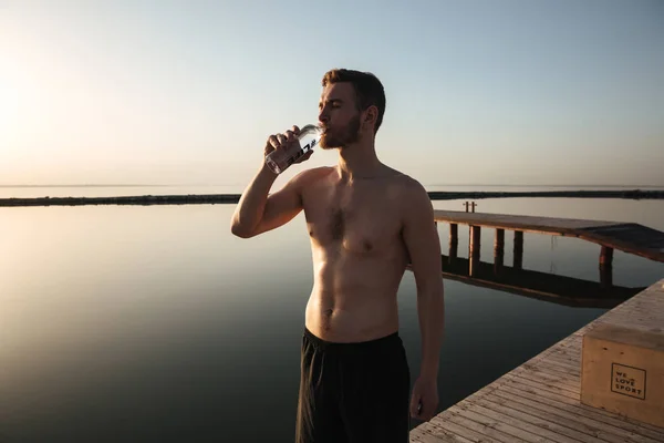 Portrait of a young tired sportsman drinking water after jogging — Stock Photo, Image