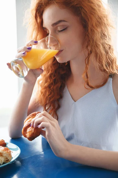 Redhead κυρία που κάθεται στο τραπέζι σε εσωτερικούς χώρους πίνοντας χυμό — Φωτογραφία Αρχείου