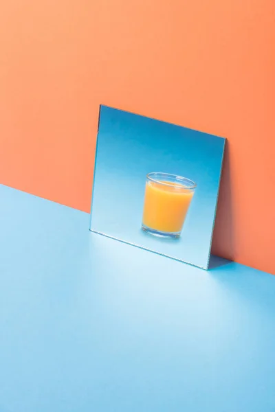 Glas juice i spegel på blå tabell isolerade — Stockfoto