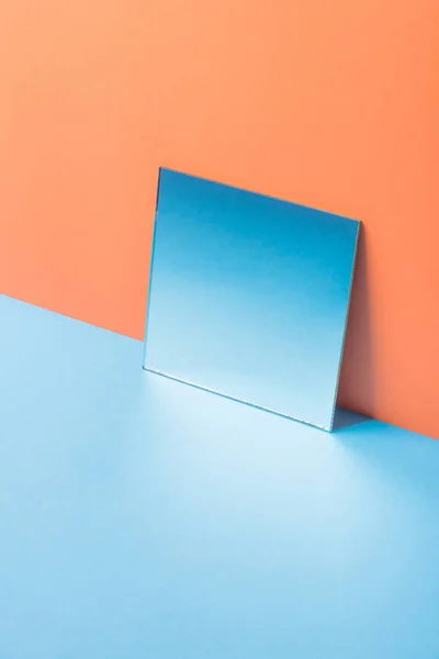 Mirror on blue table isolated over orange background — Stock Photo, Image