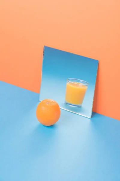 Orange près du jus dans le miroir sur la table bleue isolé — Photo