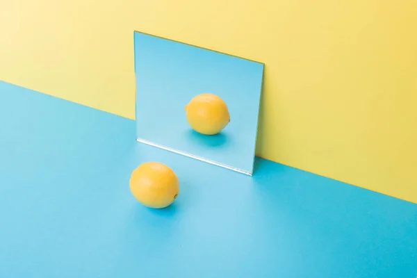 Mavi masada ayna yakınındaki sarı arka plan üzerinde izole limon — Stok fotoğraf