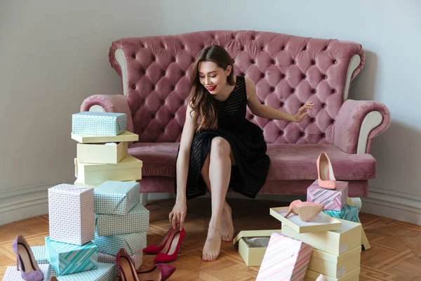 Feliz joven sentada en el sofá eligiendo zapatos . — Foto de Stock