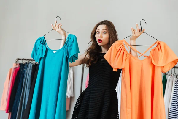 Confused young woman choosing between two dresses — Stock Photo, Image