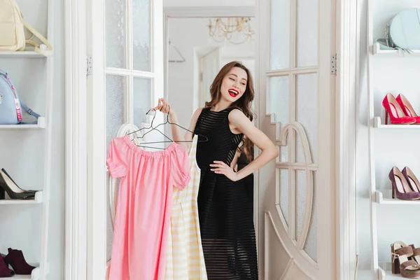 Jeune femme debout dans la boutique de vêtements à l'intérieur tenant des robes — Photo