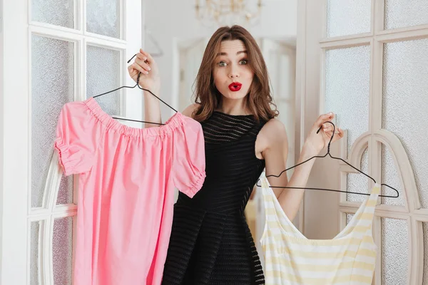 Kvinna som står inomhus att välja mellan två klänningar. — Stockfoto