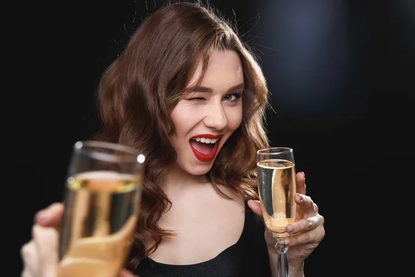 Cheerful young woman giving you glass of champagne and winking — Stock Photo, Image