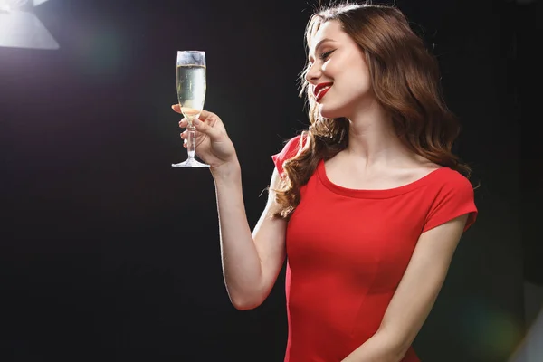 Mujer joven sonriente en vestido rojo de pie y beber champán —  Fotos de Stock