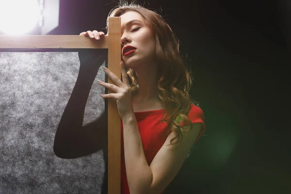 Jovem sedutora em vestido vermelho posando perto da tela dobrável — Fotografia de Stock