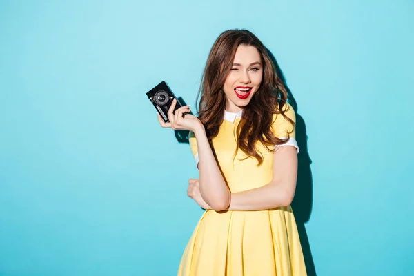 Speelse jonge vrouw in jurk retro camera houden en winking — Stockfoto