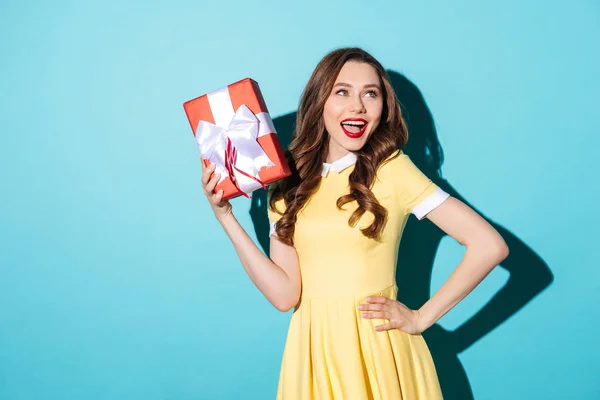 Playful girl in dress holding gift box and looking away — Stock Photo, Image