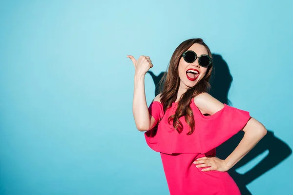 Sorrindo jovem morena apontando sobre fundo azul . — Fotografia de Stock