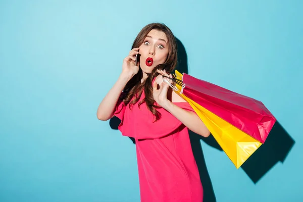 Jovem morena chocada segurando sacos de compras falando por telefone . — Fotografia de Stock