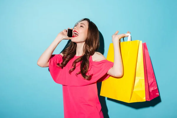 Feliz joven morena sosteniendo bolsas de compras hablando por teléfono . — Foto de Stock